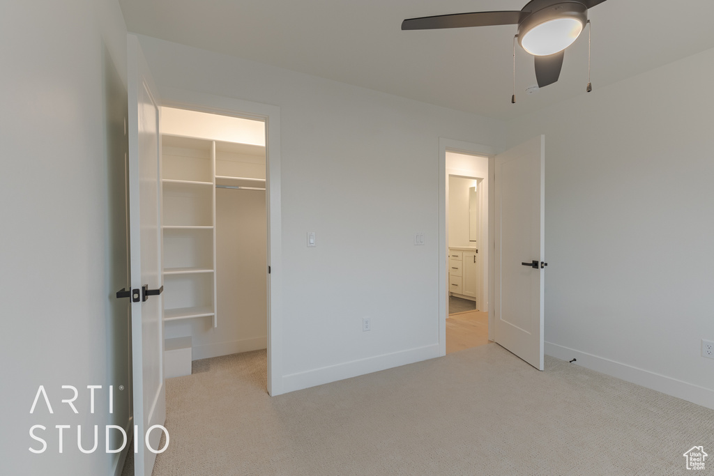 Unfurnished bedroom featuring light carpet, a closet, ceiling fan, and a walk in closet