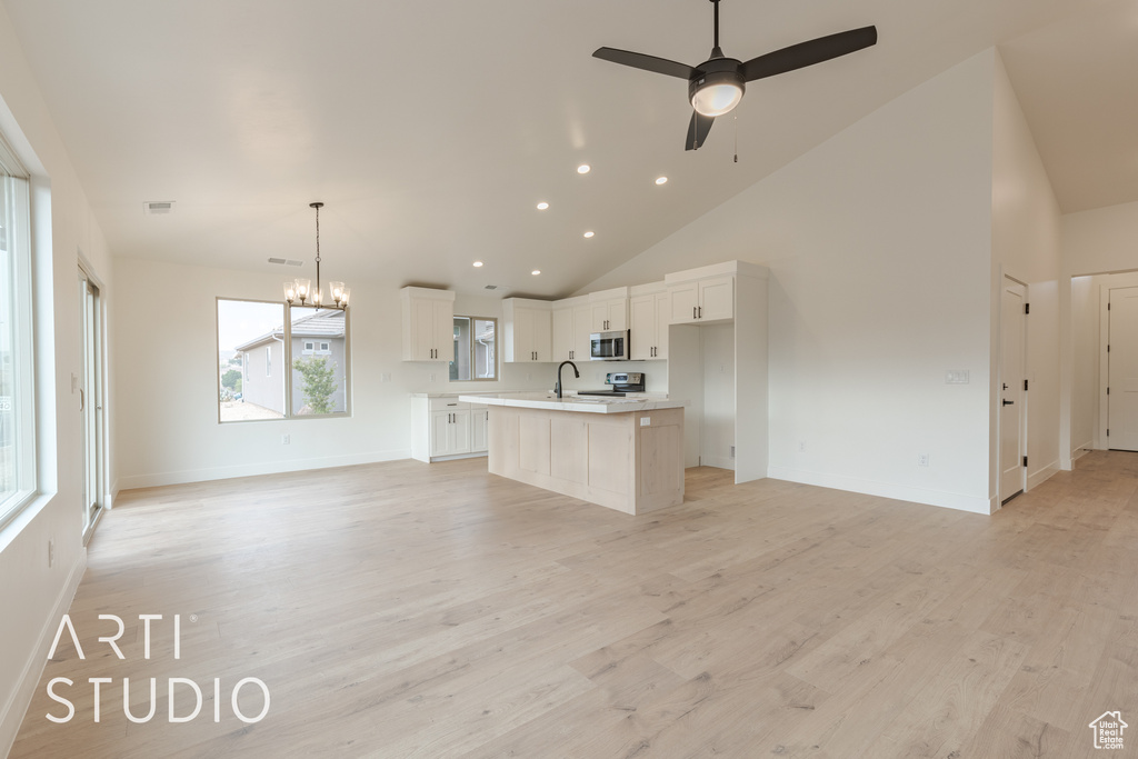 Unfurnished living room with sink, light hardwood / wood-style flooring, ceiling fan with notable chandelier, and high vaulted ceiling