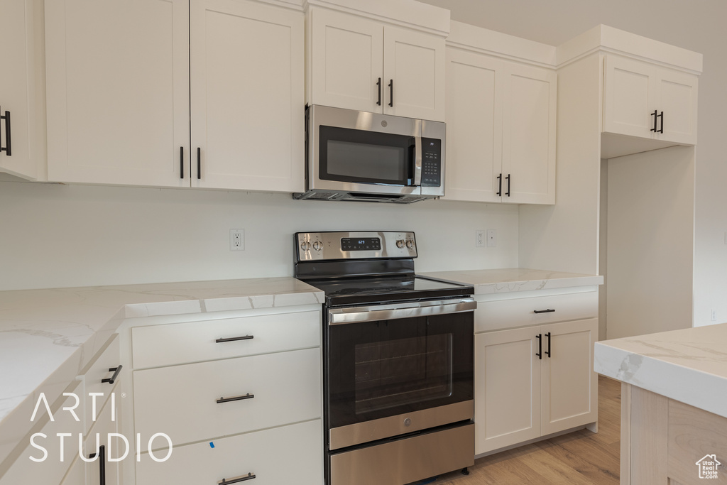 Kitchen with appliances with stainless steel finishes, white cabinets, light wood-type flooring, and light stone countertops