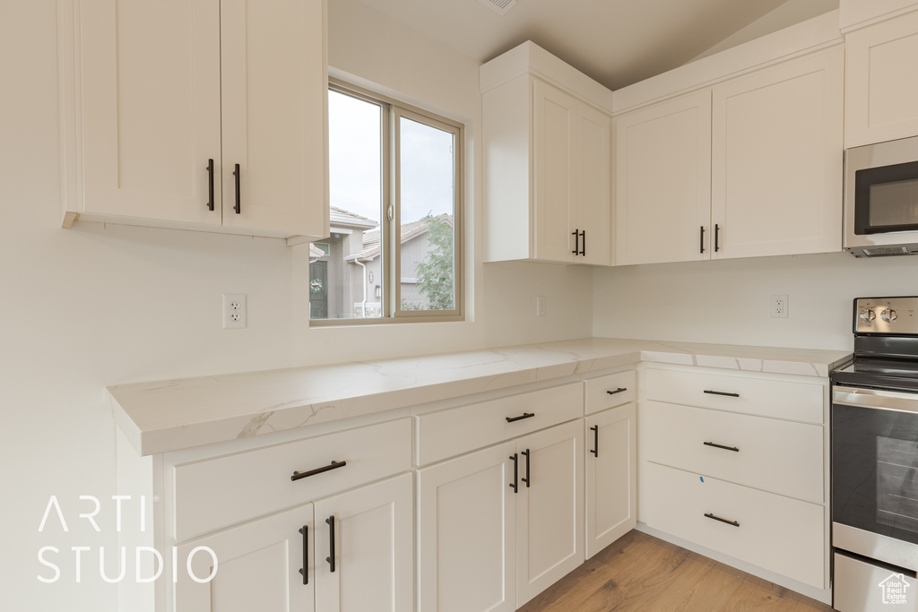 Kitchen with appliances with stainless steel finishes, light stone counters, white cabinets, and light wood-type flooring