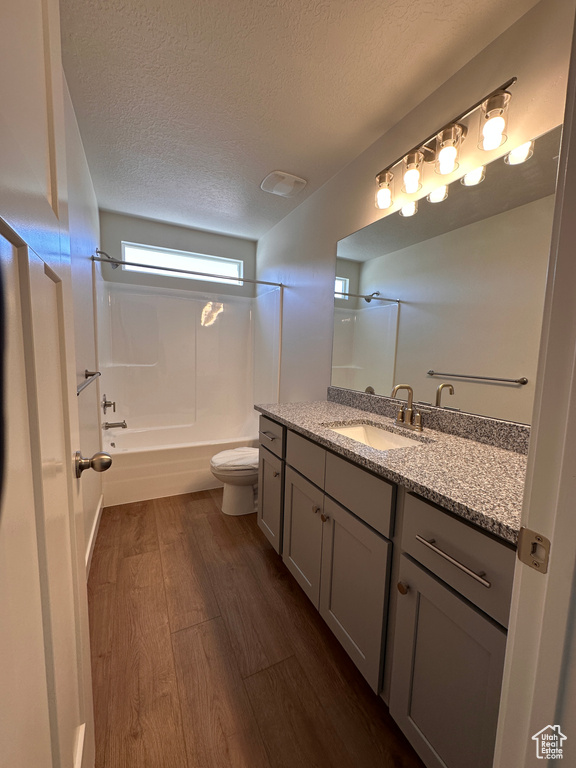 Full bathroom featuring a textured ceiling, vanity, hardwood / wood-style floors, toilet, and shower / bathtub combination