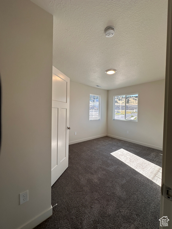 Unfurnished room with a textured ceiling and dark colored carpet