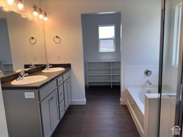 Bathroom with tiled tub, hardwood / wood-style flooring, and dual bowl vanity