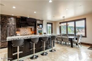 Kitchen with dark brown cabinets, light tile patterned floors, backsplash, hanging light fixtures, and a kitchen bar