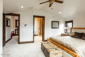 Carpeted bedroom featuring ceiling fan and vaulted ceiling