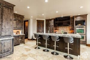 Kitchen featuring dark brown cabinets, tasteful backsplash, stainless steel double oven, a breakfast bar, and light tile patterned floors