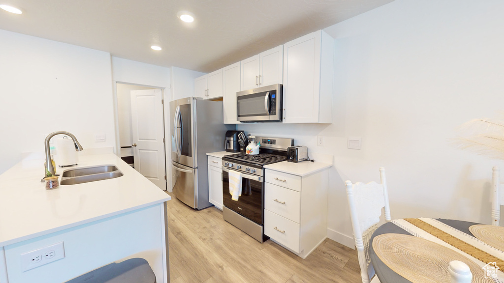 Kitchen with sink, appliances with stainless steel finishes, light hardwood / wood-style floors, and white cabinetry