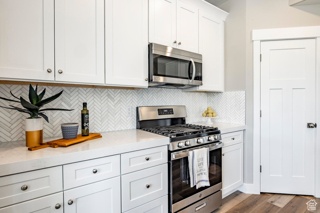 Kitchen with tasteful backsplash, stainless steel appliances, white cabinets, light hardwood / wood-style floors, and light stone countertops