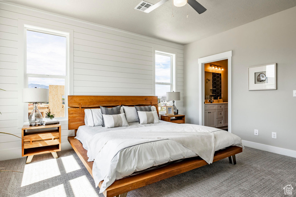 Carpeted bedroom with multiple windows, ensuite bath, and ceiling fan