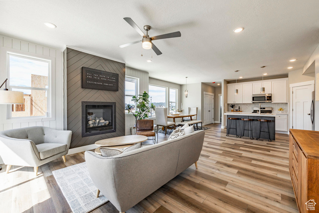 Living room with ceiling fan, light hardwood / wood-style flooring, wooden walls, and a large fireplace