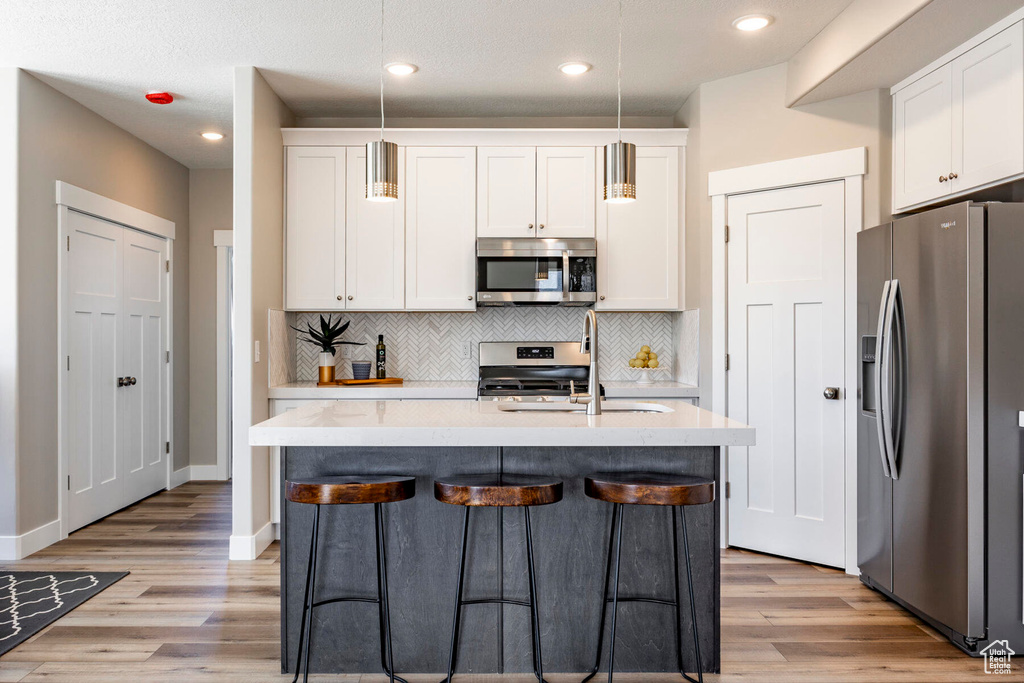 Kitchen featuring appliances with stainless steel finishes, backsplash, pendant lighting, and light wood-type flooring