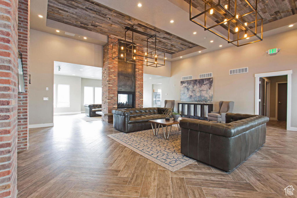 Living room with parquet flooring, a brick fireplace, brick wall, a towering ceiling, and a raised ceiling