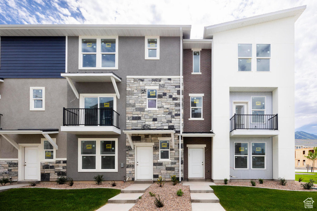 Townhome / multi-family property featuring a balcony and a front yard