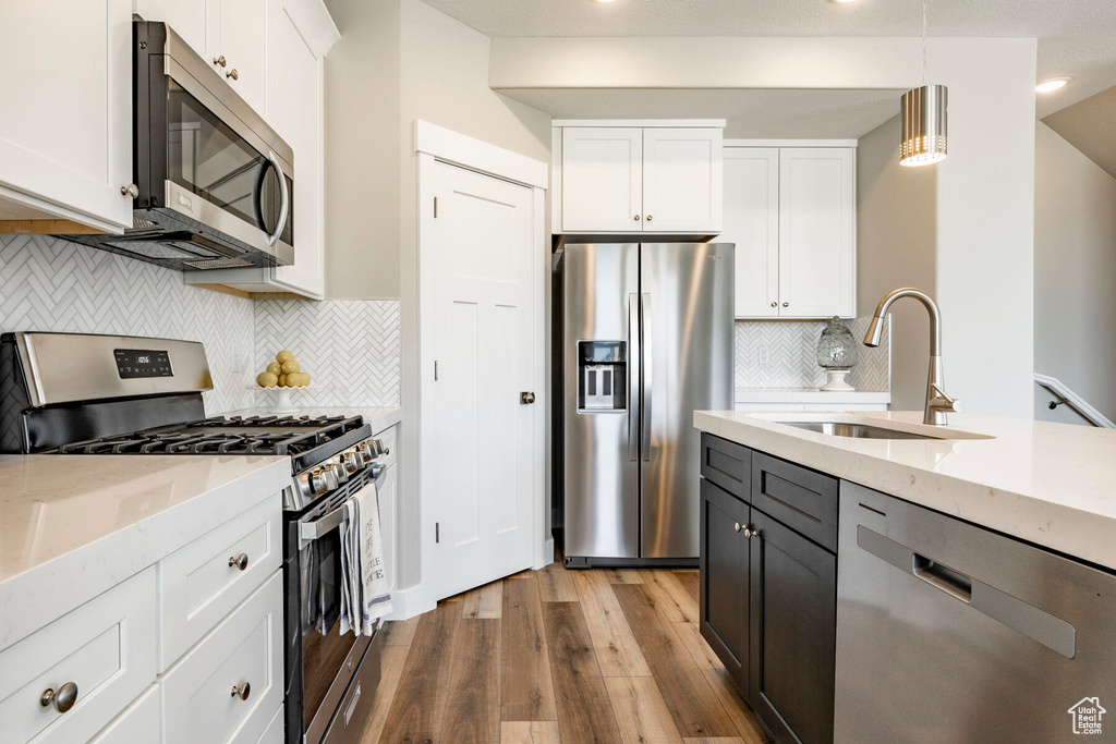 Kitchen featuring light hardwood / wood-style flooring, white cabinets, tasteful backsplash, and stainless steel appliances