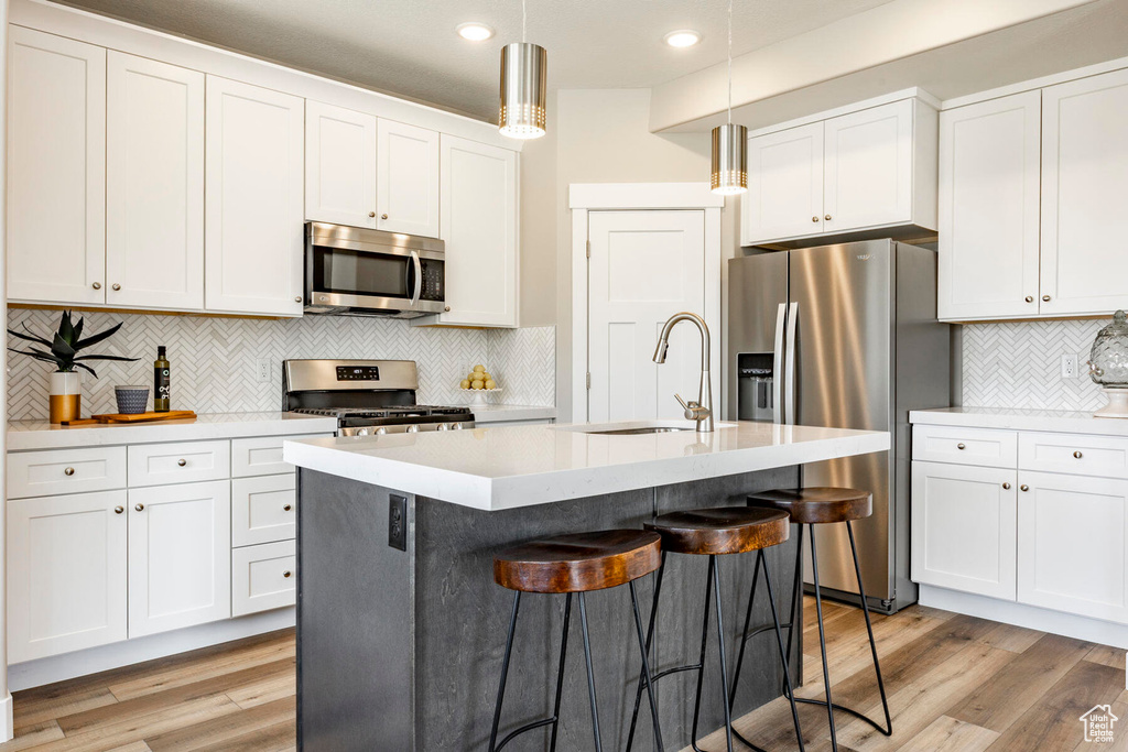 Kitchen featuring tasteful backsplash, light hardwood / wood-style floors, appliances with stainless steel finishes, and a center island with sink