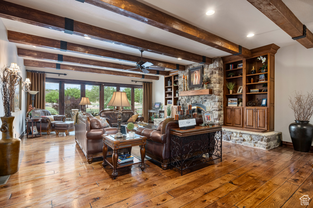 Living room with hardwood / wood-style flooring, a stone fireplace, ceiling fan, and plenty of natural light