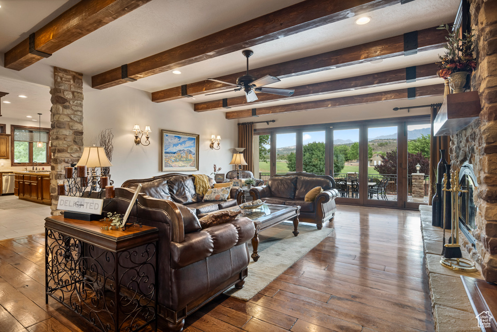 Living room with hardwood / wood-style flooring, ceiling fan, beamed ceiling, sink, and a stone fireplace