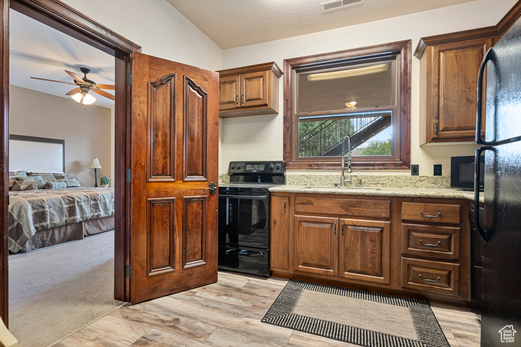 Kitchen with ceiling fan, black appliances, light stone countertops, light carpet, and vaulted ceiling