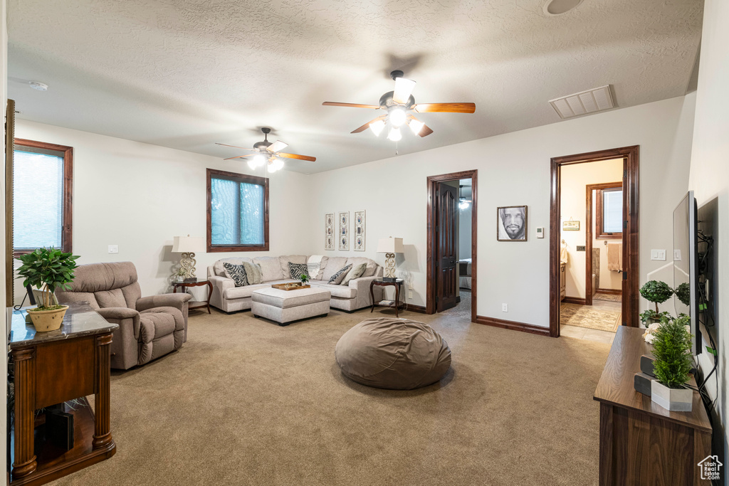 Living room featuring a textured ceiling, light colored carpet, and ceiling fan