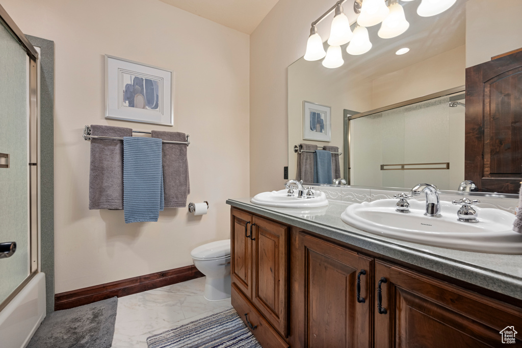 Full bathroom featuring tile patterned floors, double sink vanity, toilet, and enclosed tub / shower combo