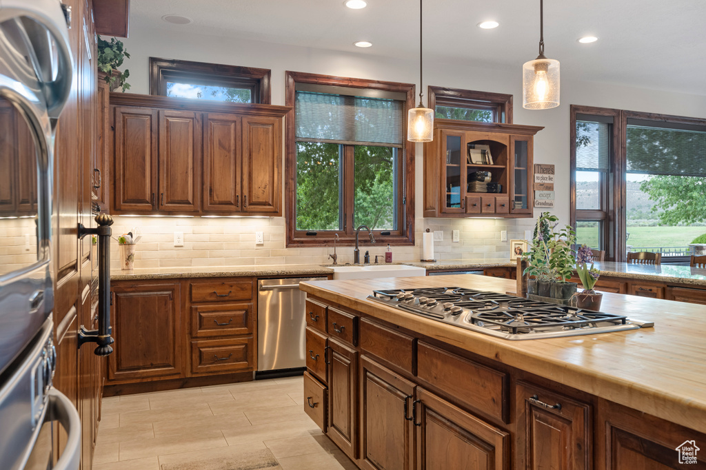 Kitchen with stainless steel appliances, wood counters, sink, hanging light fixtures, and decorative backsplash