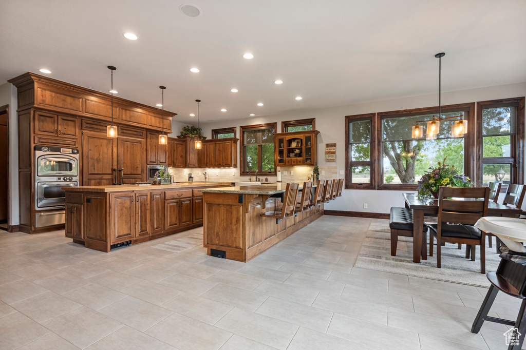 Kitchen featuring double oven, a healthy amount of sunlight, light tile patterned floors, and a kitchen island