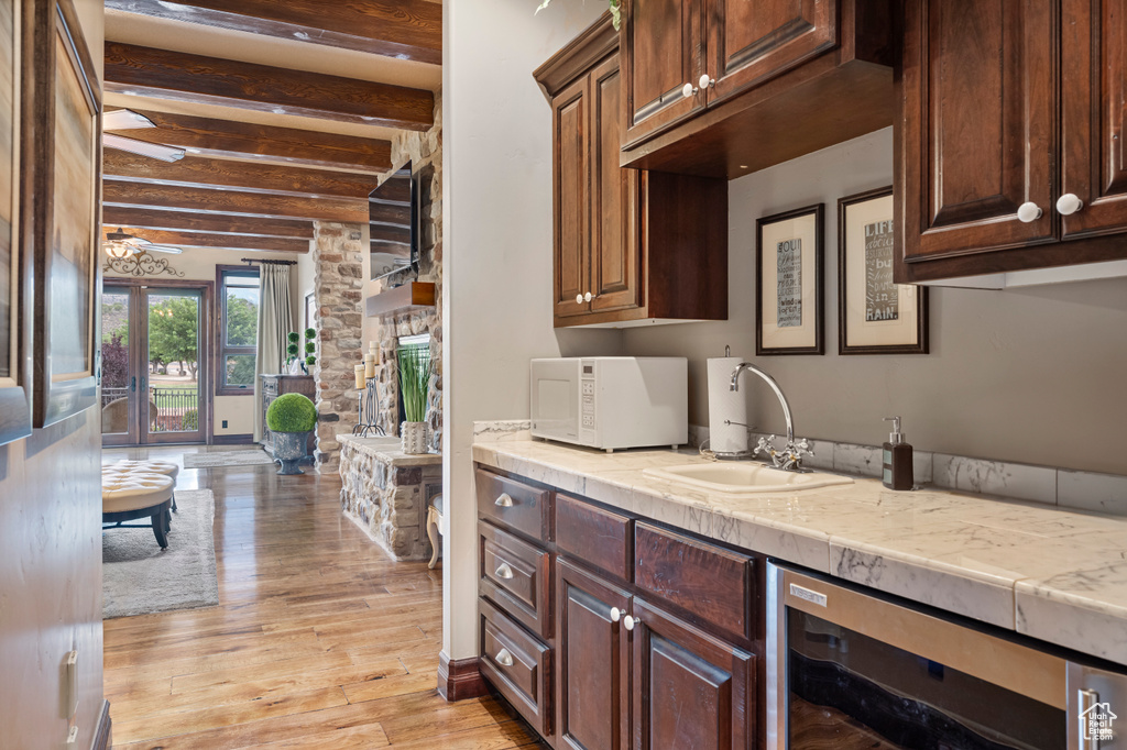 Kitchen featuring beamed ceiling, sink, light hardwood / wood-style floors, ceiling fan, and wine cooler