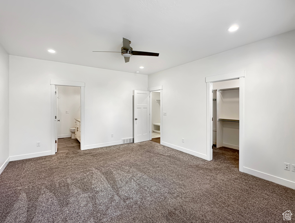 Unfurnished bedroom featuring a walk in closet, a closet, ensuite bathroom, carpet flooring, and ceiling fan