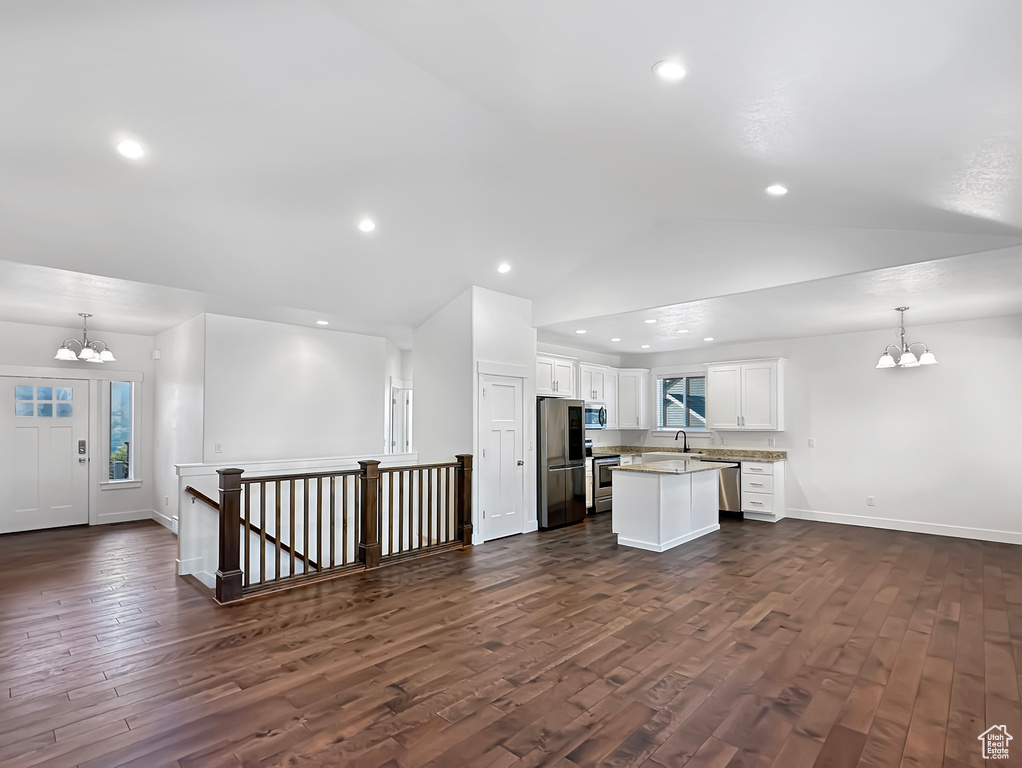 Unfurnished living room featuring dark hardwood / wood-style flooring, sink, a notable chandelier, and lofted ceiling