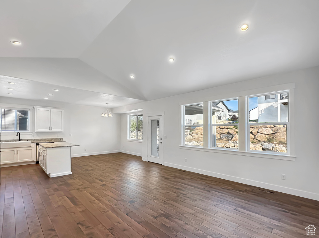 Unfurnished living room featuring vaulted ceiling, a notable chandelier, and dark hardwood / wood-style flooring