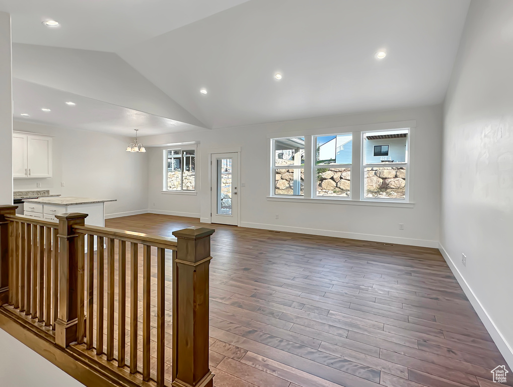 Unfurnished living room with hardwood / wood-style floors, an inviting chandelier, and vaulted ceiling