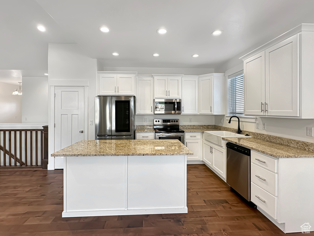 Kitchen with a center island, sink, light stone countertops, dark hardwood / wood-style floors, and appliances with stainless steel finishes