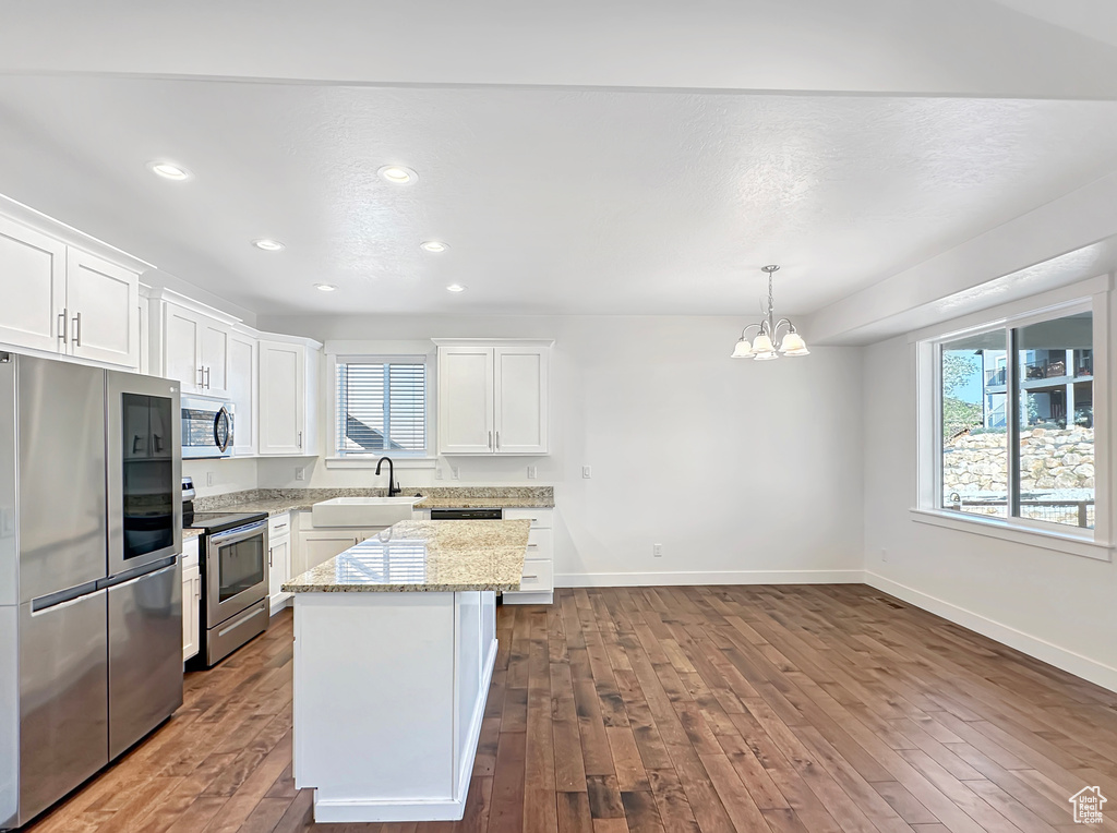 Kitchen with hardwood / wood-style floors, light stone countertops, appliances with stainless steel finishes, and white cabinetry