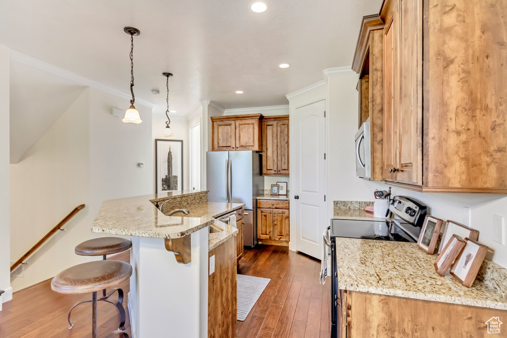 Kitchen featuring dark wood-type flooring, light stone counters, electric range oven, hanging light fixtures, and a center island with sink