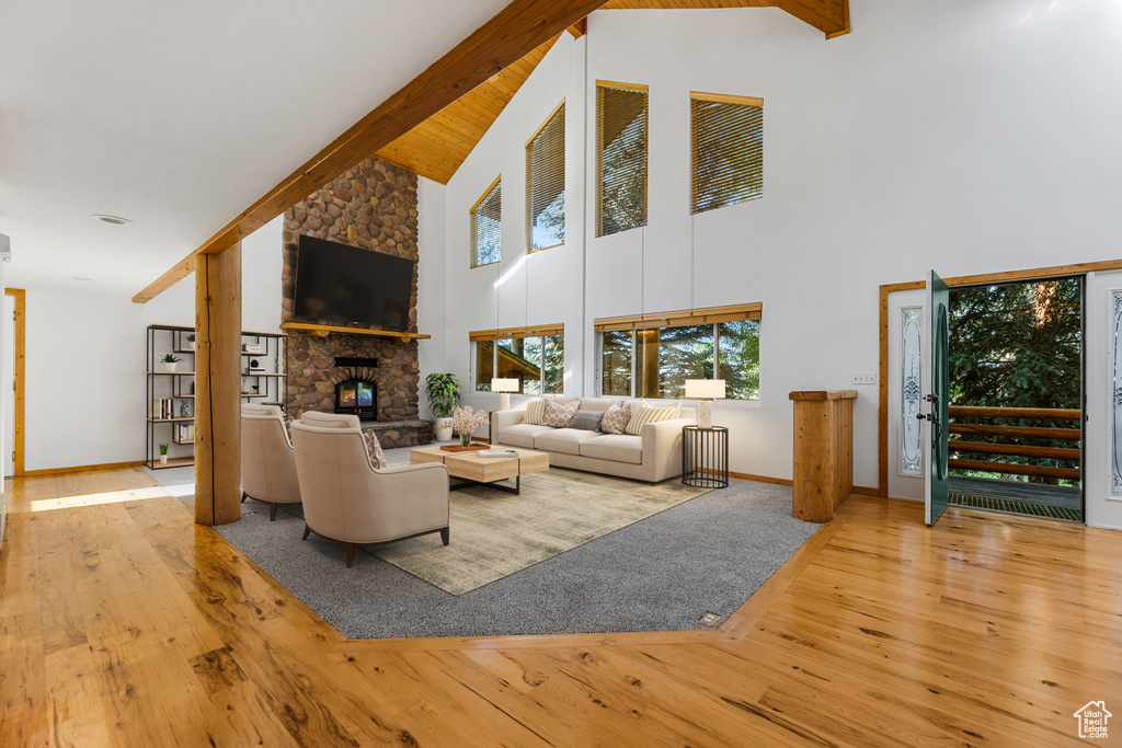 Living room with light hardwood / wood-style floors, beam ceiling, a stone fireplace, and high vaulted ceiling