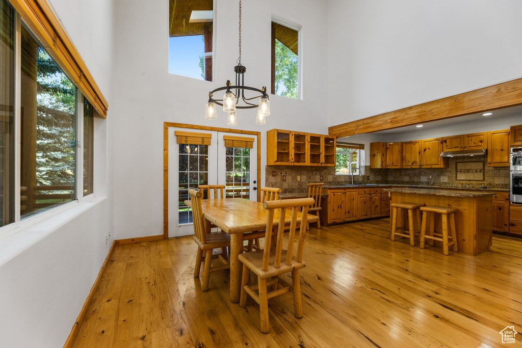 Dining area with french doors, light wood-type flooring, an inviting chandelier, a high ceiling, and sink