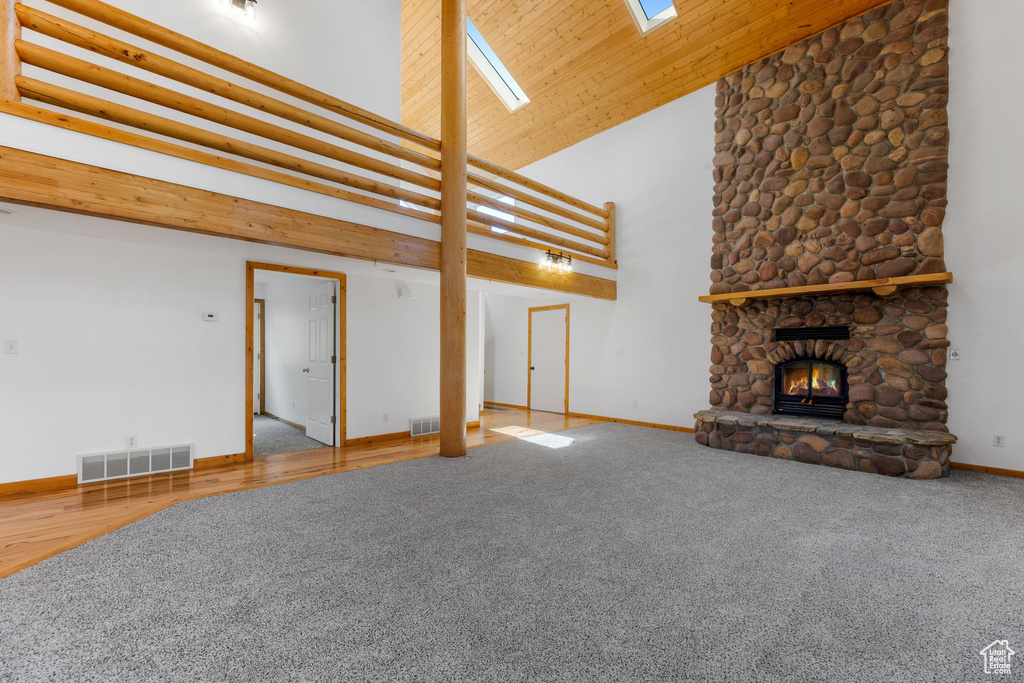 Unfurnished living room featuring a skylight, wood ceiling, a fireplace, carpet, and high vaulted ceiling