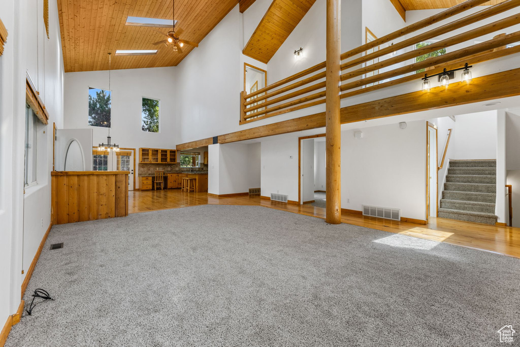 Unfurnished living room featuring a skylight, light hardwood / wood-style flooring, wooden ceiling, and high vaulted ceiling