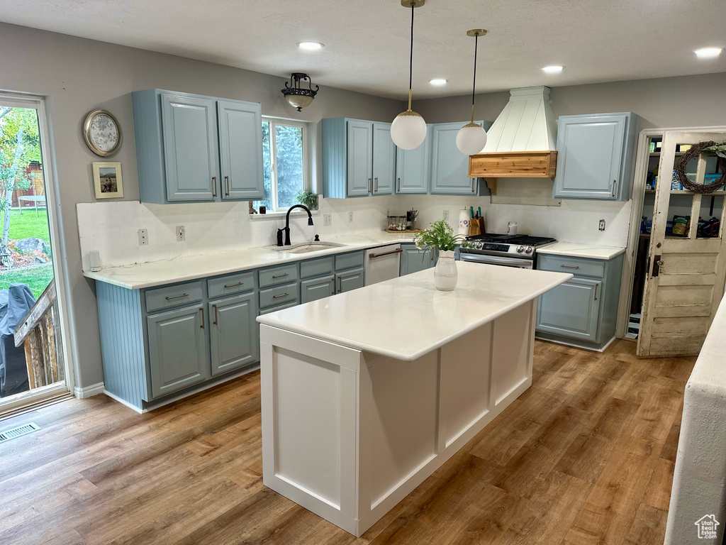 Kitchen with pendant lighting, appliances with stainless steel finishes, custom range hood, and wood-type flooring