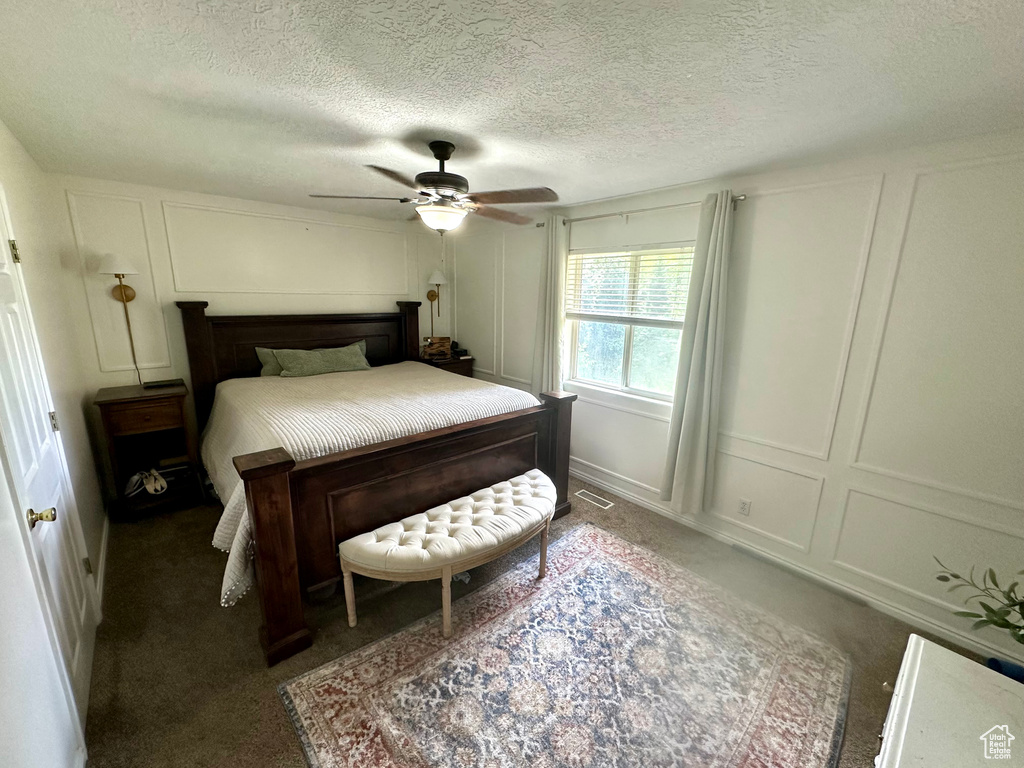 Bedroom with a textured ceiling, dark carpet, and ceiling fan