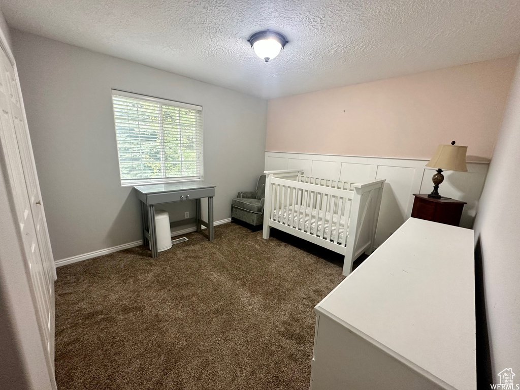 Carpeted bedroom featuring a nursery area and a textured ceiling