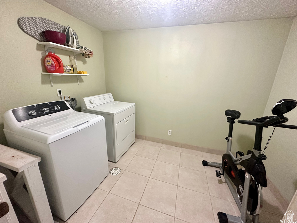 Clothes washing area featuring washer and clothes dryer, a textured ceiling, and light tile patterned floors