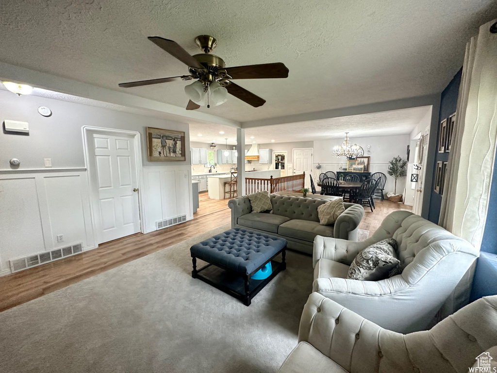 Living room with ceiling fan with notable chandelier, light hardwood / wood-style flooring, and a textured ceiling