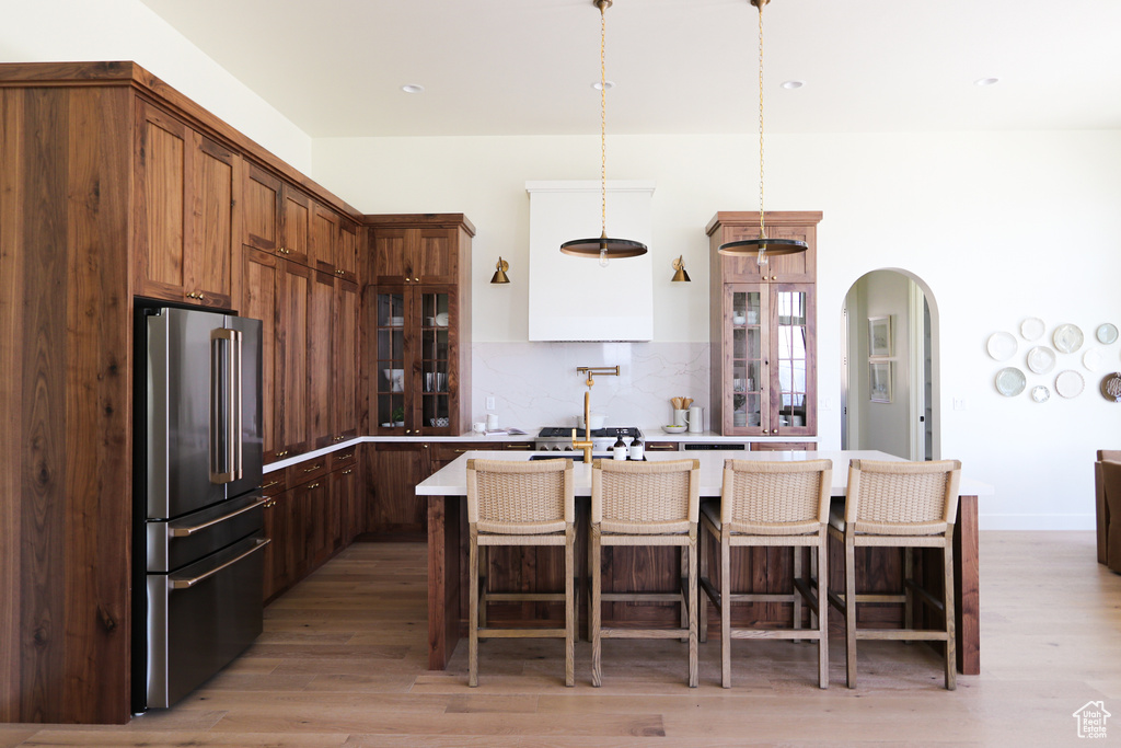 Kitchen with tasteful backsplash, light wood-type flooring, a kitchen island, high end fridge, and decorative light fixtures