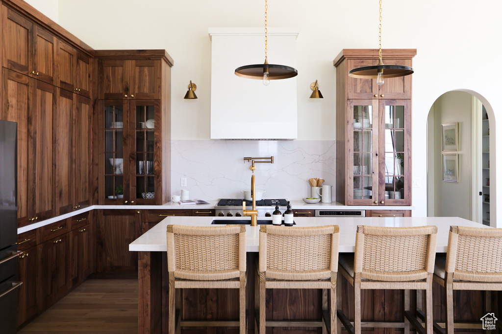 Kitchen with a breakfast bar, tasteful backsplash, dark hardwood / wood-style flooring, a kitchen island with sink, and decorative light fixtures