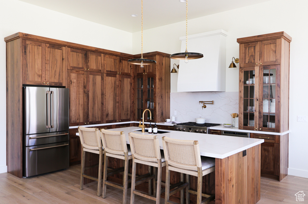 Kitchen with backsplash, high quality fridge, hardwood / wood-style floors, and an island with sink