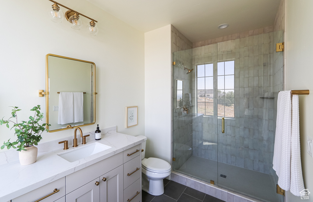 Bathroom with a shower with door, vanity, tile patterned flooring, and toilet