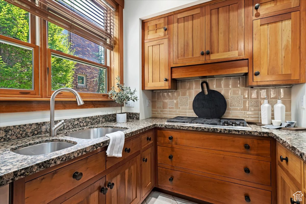 Kitchen with premium range hood, stone countertops, stainless steel gas stovetop, and sink