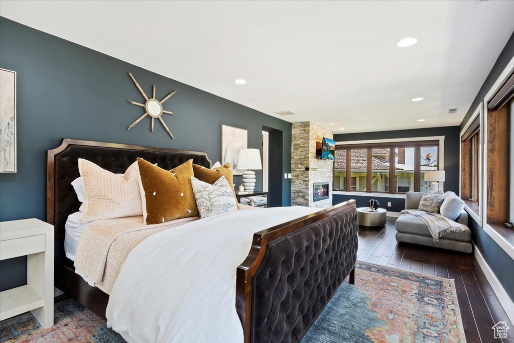 Bedroom with ceiling fan, dark hardwood / wood-style flooring, and a stone fireplace