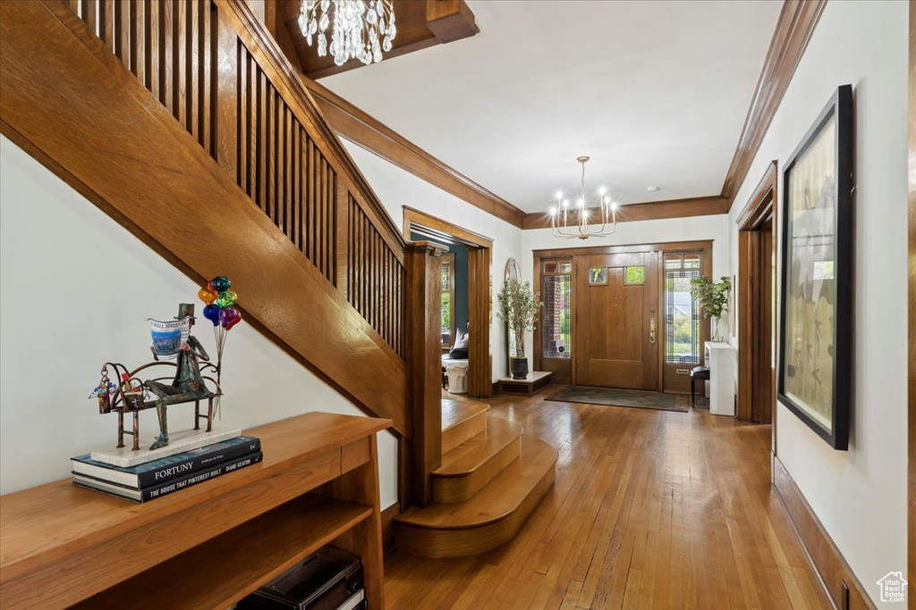 Foyer entrance with crown molding, an inviting chandelier, and hardwood / wood-style flooring